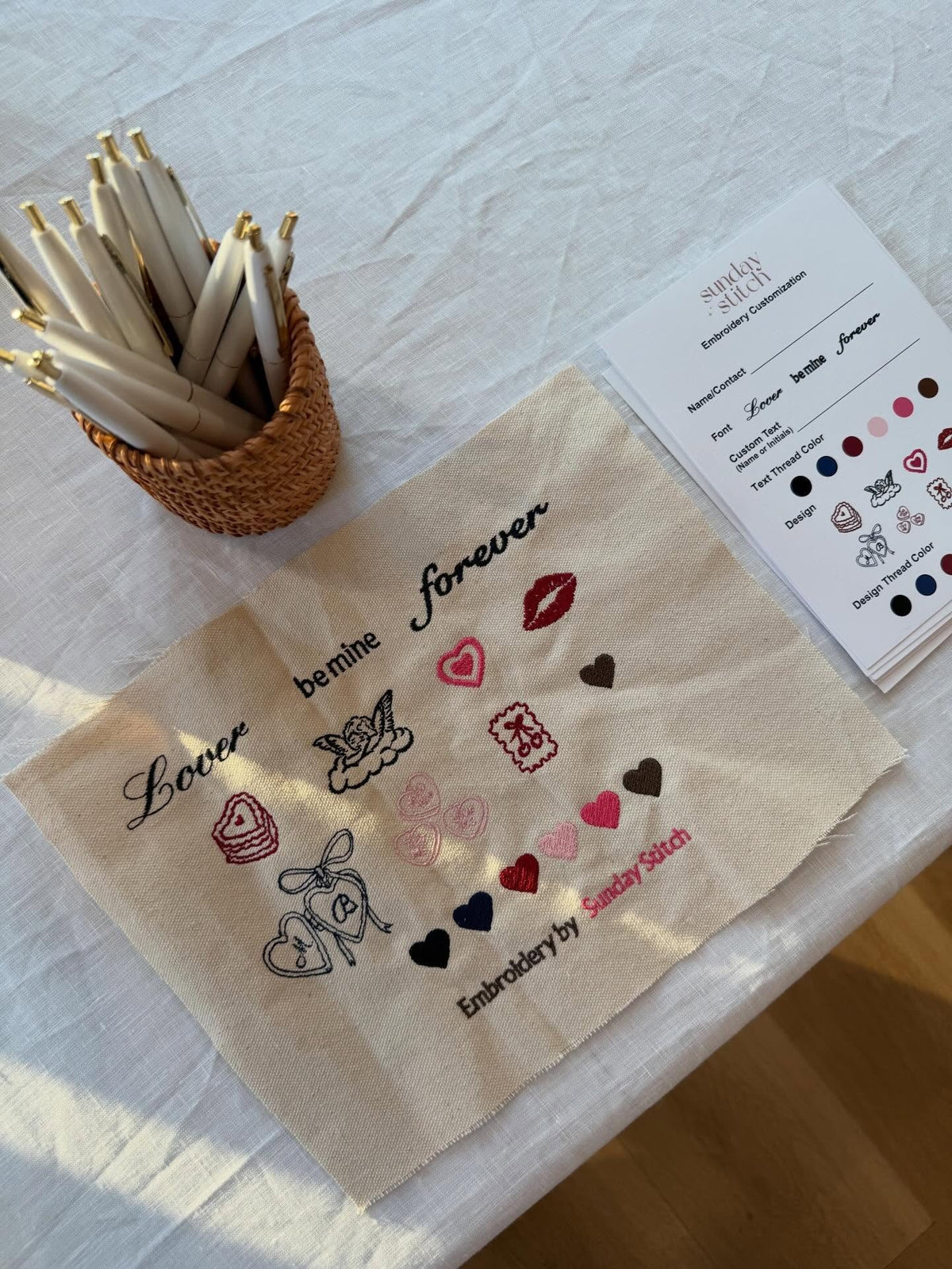 Embroidery design sheet with various patterns and a small basket of embroidery threads on a light fabric background.