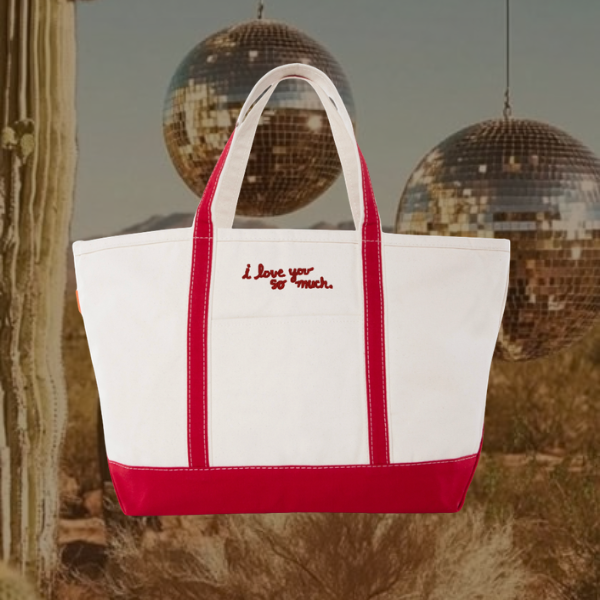 A white canvas tote bag with red trim and red handles, featuring the embroidered red text 'I love you so much.' on the front, set against a desert background with cacti and hanging disco balls.