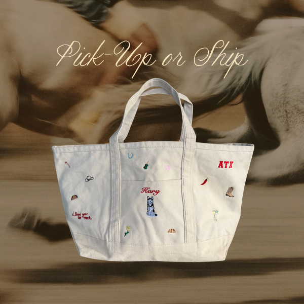 A white canvas tote bag with embroidered details and text, shown against a blurred background of a person and a horse with the text 'Pick-Up or Ship' written above.